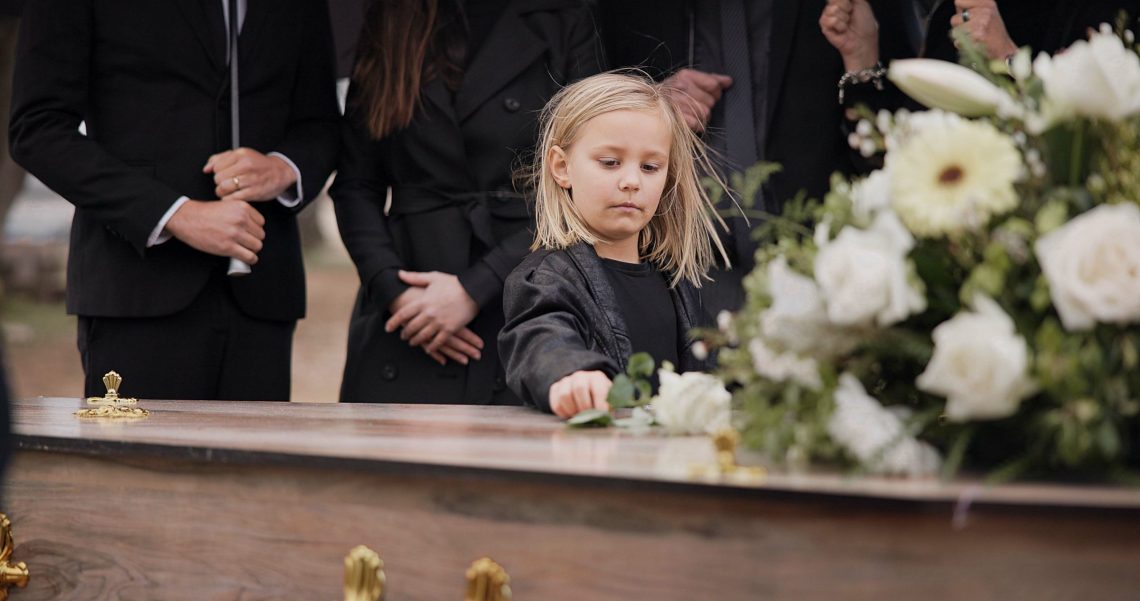 death, grief and girl at funeral with flower on coffin, family and sad child at service in graveyard for respect. roses, loss and people at wood casket in cemetery with kid crying at grave for burial