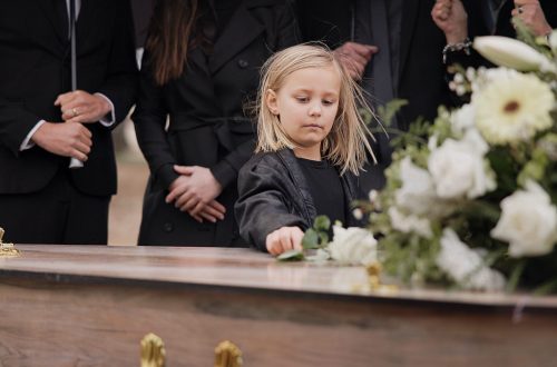 death, grief and girl at funeral with flower on coffin, family and sad child at service in graveyard for respect. roses, loss and people at wood casket in cemetery with kid crying at grave for burial