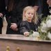death, grief and girl at funeral with flower on coffin, family and sad child at service in graveyard for respect. roses, loss and people at wood casket in cemetery with kid crying at grave for burial