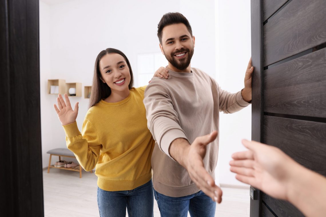 happy couple welcoming their guest near door. invitation to come indoors