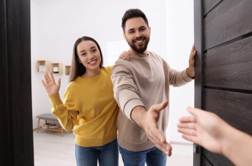 happy couple welcoming their guest near door. invitation to come indoors