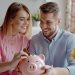 smiling, happy young family together put coins in piggy bank to save money. married couple are planning to save up finances. savings, investments, financial freedom, business, hope for success